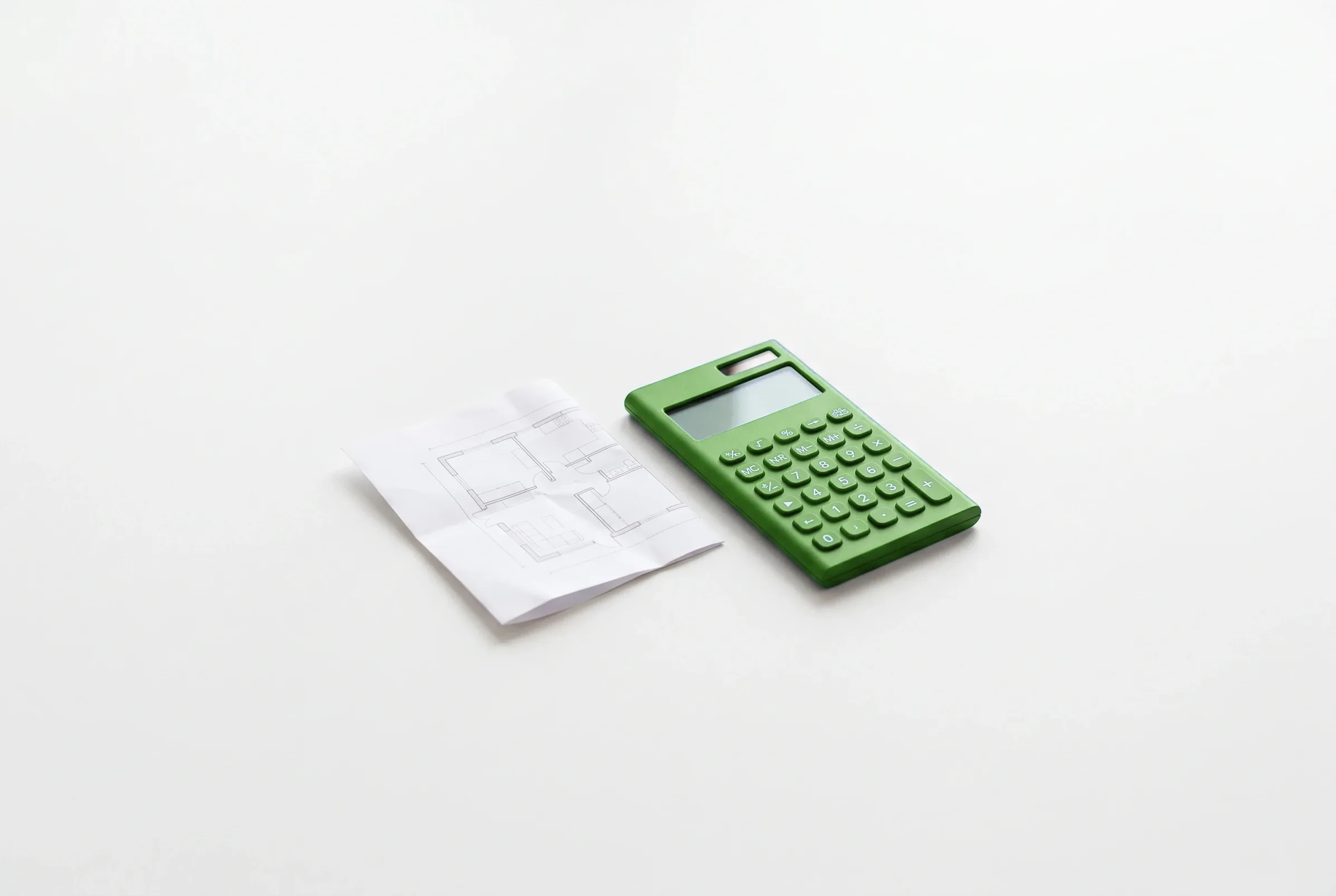 Calculadora verde junto a un plano arquitectónico doblado sobre una superficie blanca.