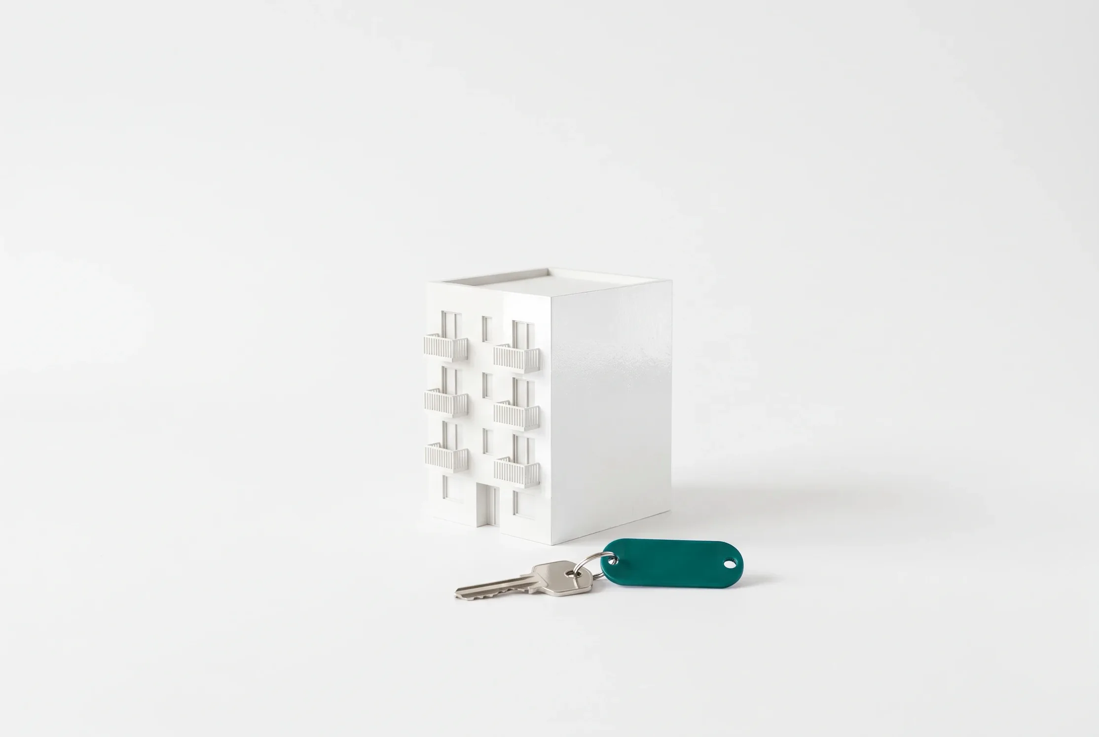 Maqueta blanca de un edificio de apartamentos con una llave de llavero verde azulado delante.