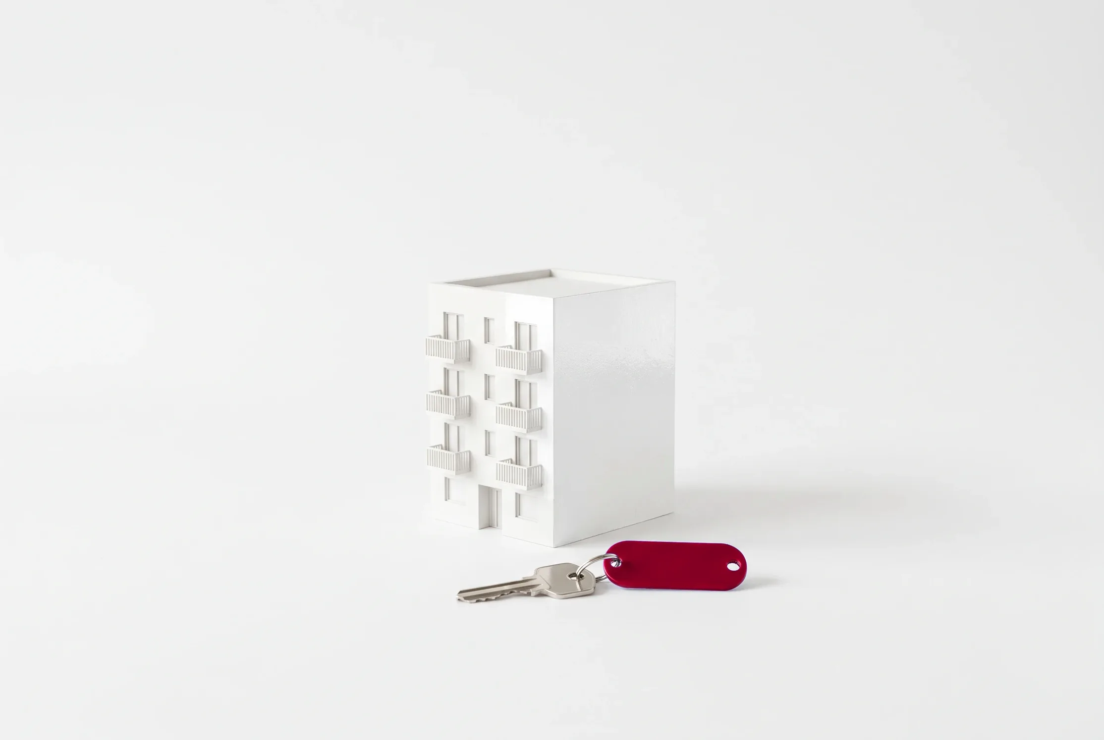 Maqueta blanca de un edificio de apartamentos con una llave de llavero rojo delante.