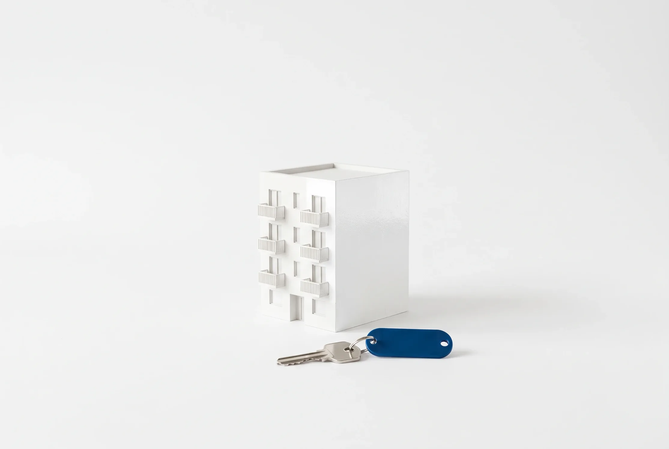Maqueta blanca de un edificio de apartamentos con una llave de llavero azul delante.