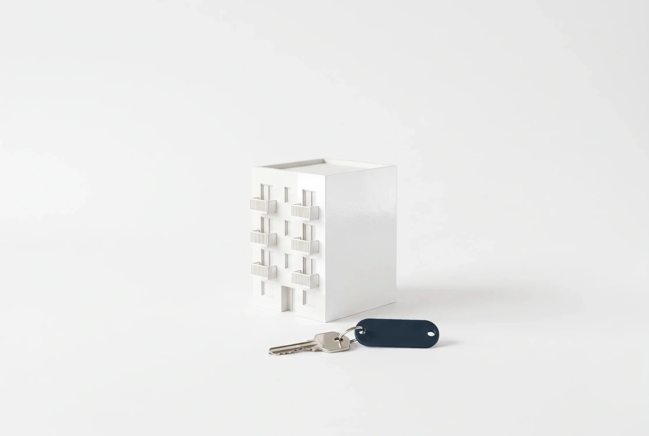 Maqueta blanca de un edificio de apartamentos con una llave de llavero gris pizarra delante.
