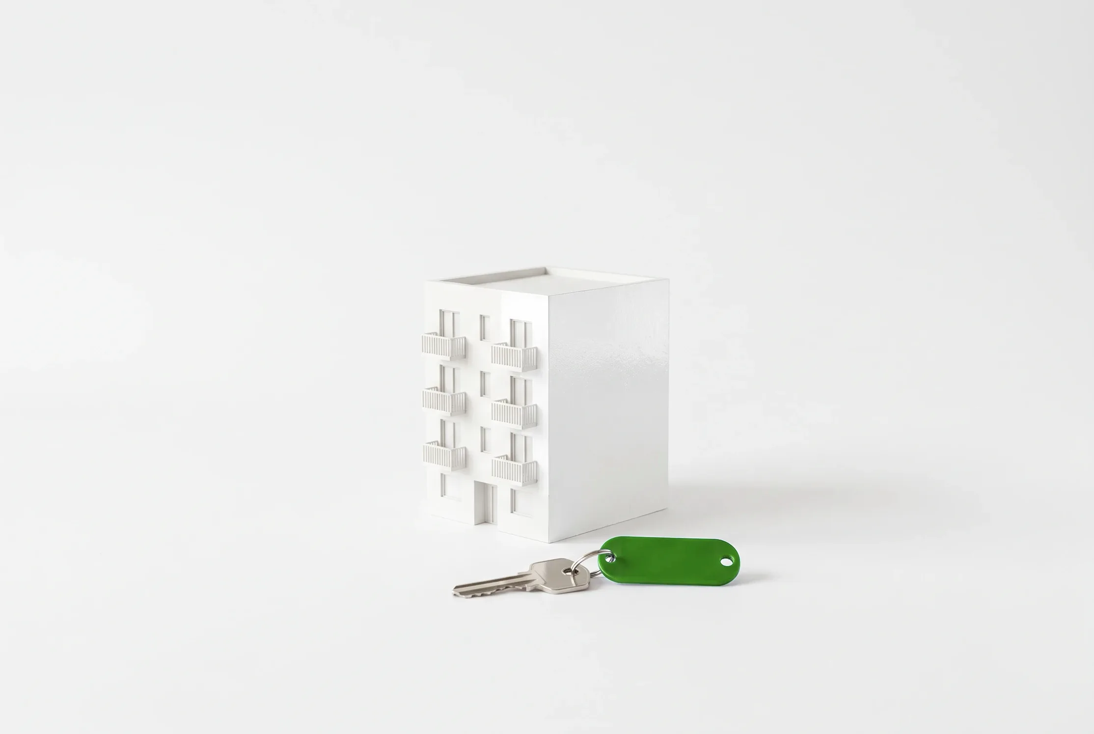 Maqueta blanca de un edificio de apartamentos con una llave de llavero verde delante.