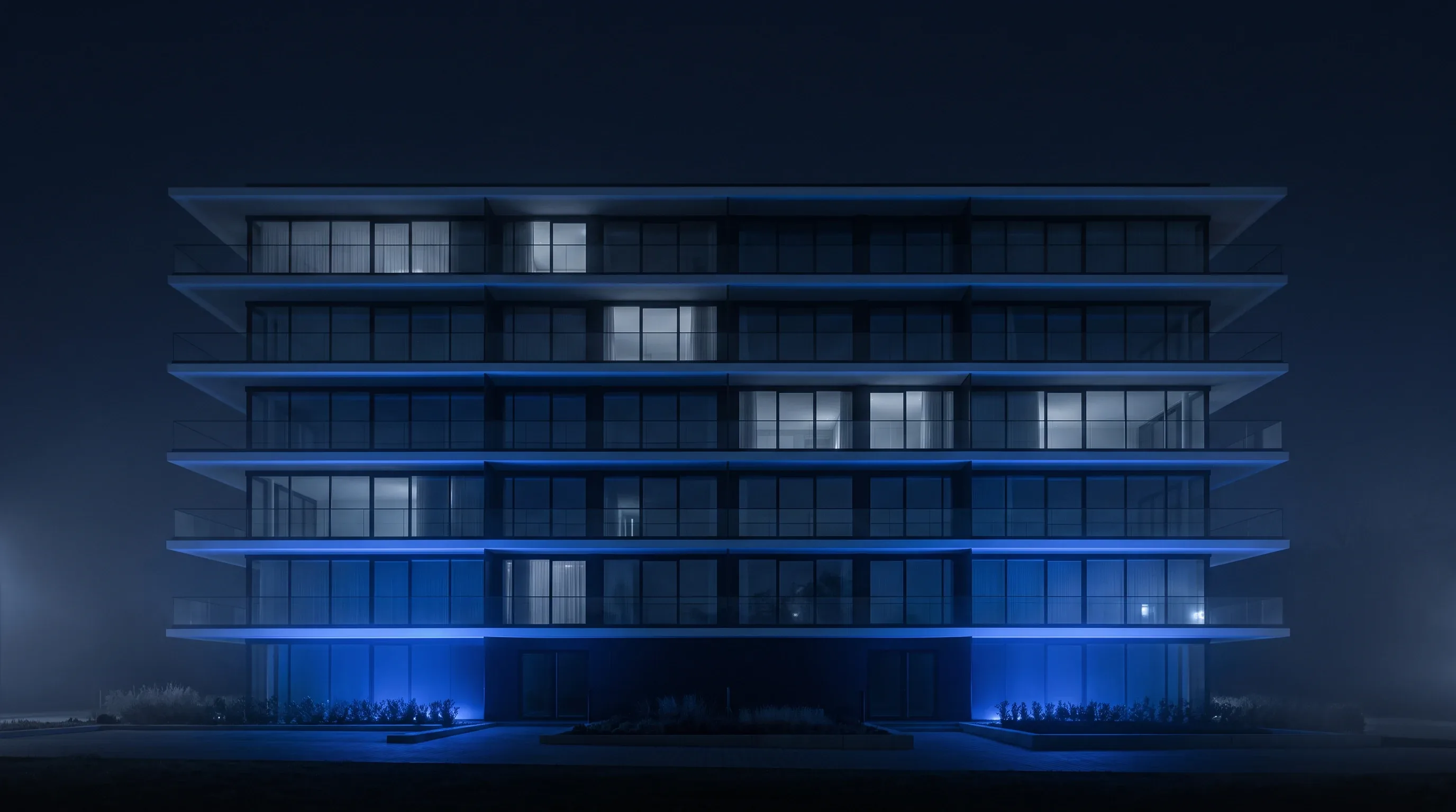 Edificio residencial terminado con fachada de vidrio, visto de frente e iluminado en azul.